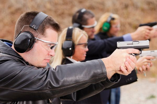 Group of people at a shooting range wearing safety gear and aiming handguns during firearm training