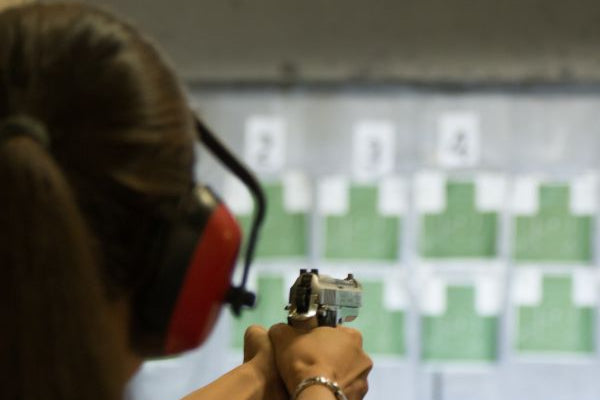 Woman wearing ear protection aiming a handgun at targets in an indoor shooting range.