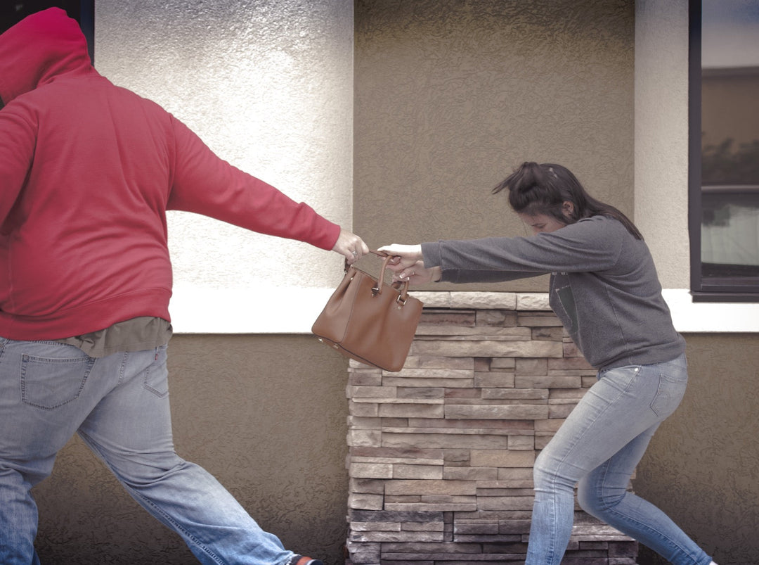 man in red hoody and blue jeans taking the purse of a women in a gray shirt and blue jeans
