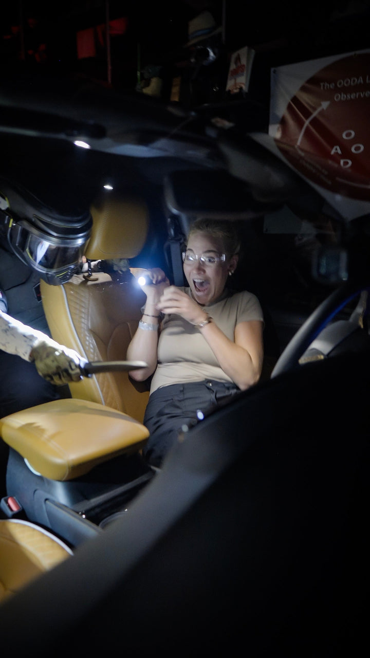 Person inside a vehicle holding a flashlight, looking surprised or scared.
