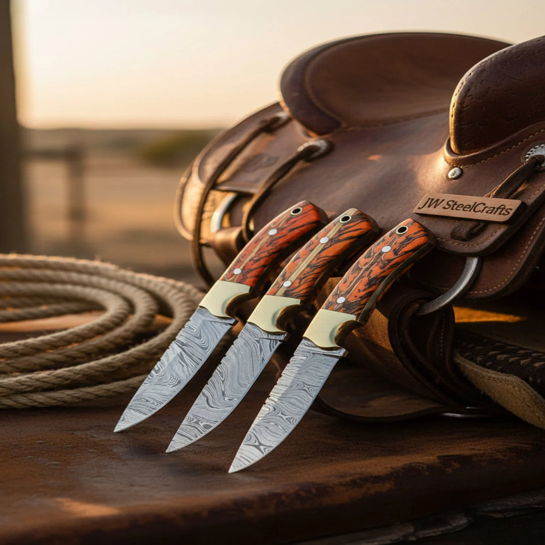 Three knives with wooden handles on a leather saddle blanket with 'JW SteelCrafts' branding.