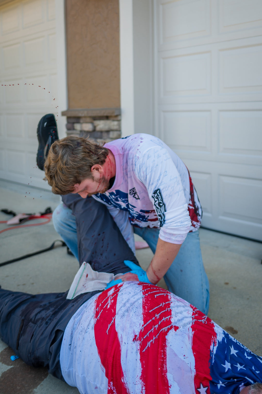 Man simulating applying pressure to a wound on a man with an American flag shirt on.
