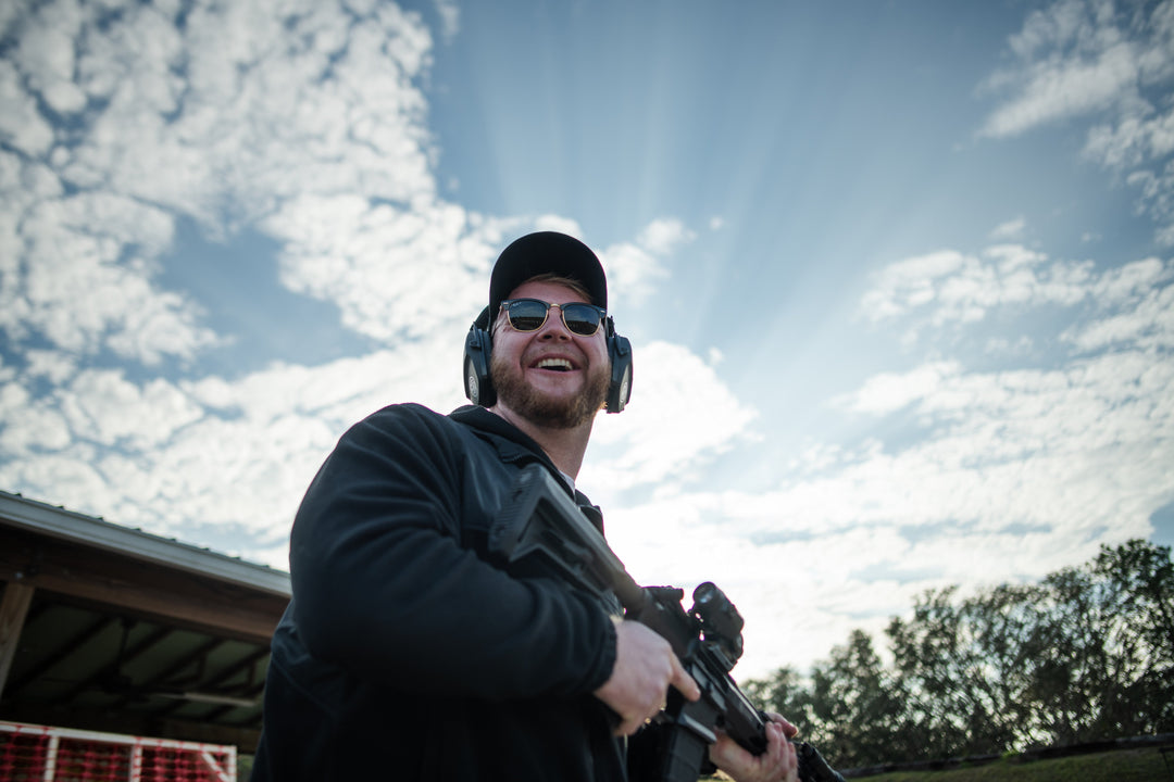 Man holding a rifle with ear protection against a cloudy sky