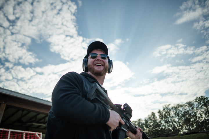 Man holding a rifle with ear protection against a cloudy sky