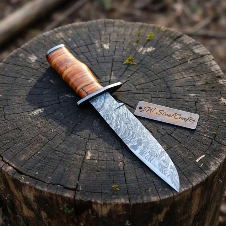 Knife with wooden handle and metal blade on a tree stump, branded 'JW SteelCrafts'.