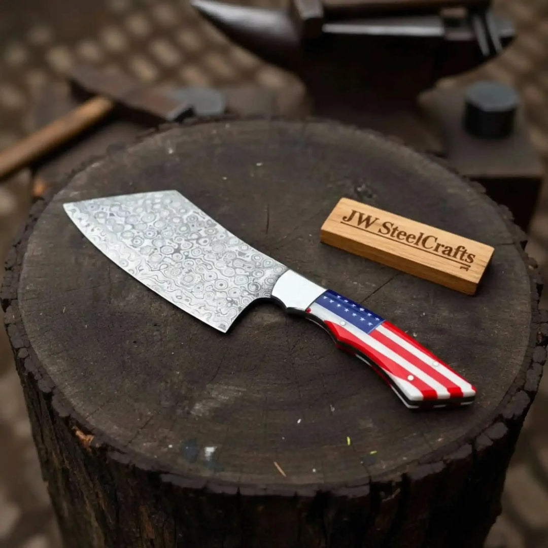 Cleaver knife with a decorative blade and American flag handle on a tree stump, branded 'JW SteelCrafts'.