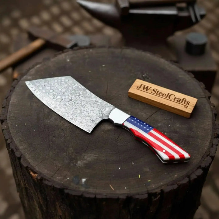 Cleaver knife with a decorative blade and American flag handle on a tree stump, branded 'JW SteelCrafts'.