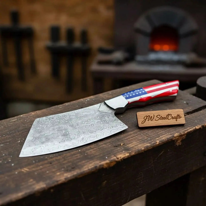 Cleaver knife with a decorative blade and american flag handle laying on a wooden block, branded 'JW SteelCrafts'.