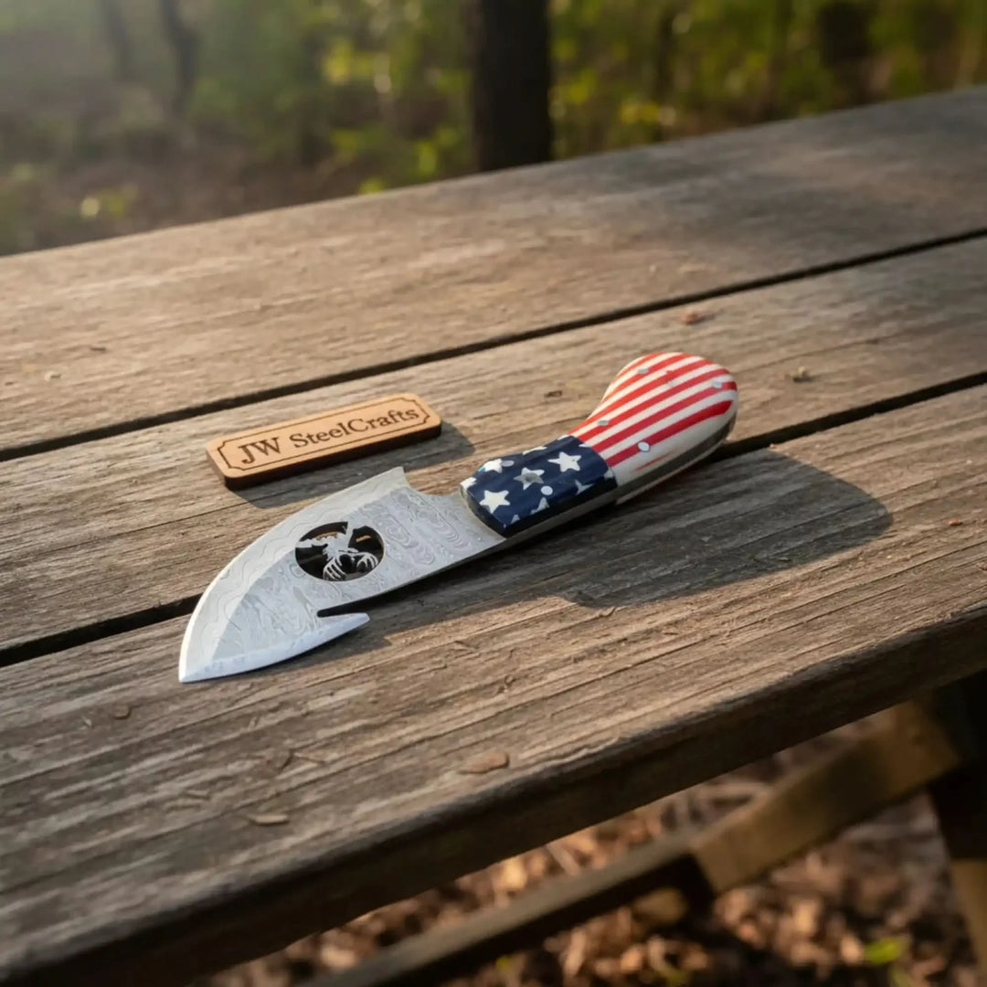 Knife with American flag handle on a wooden surface, next to a 'JW SteelCrafts' logo.