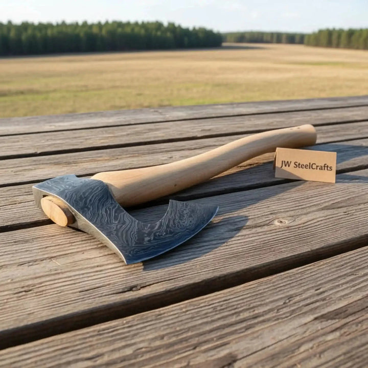 Axes on a wooden surface with a 'JW SteelCrafts' label in the background of a field.