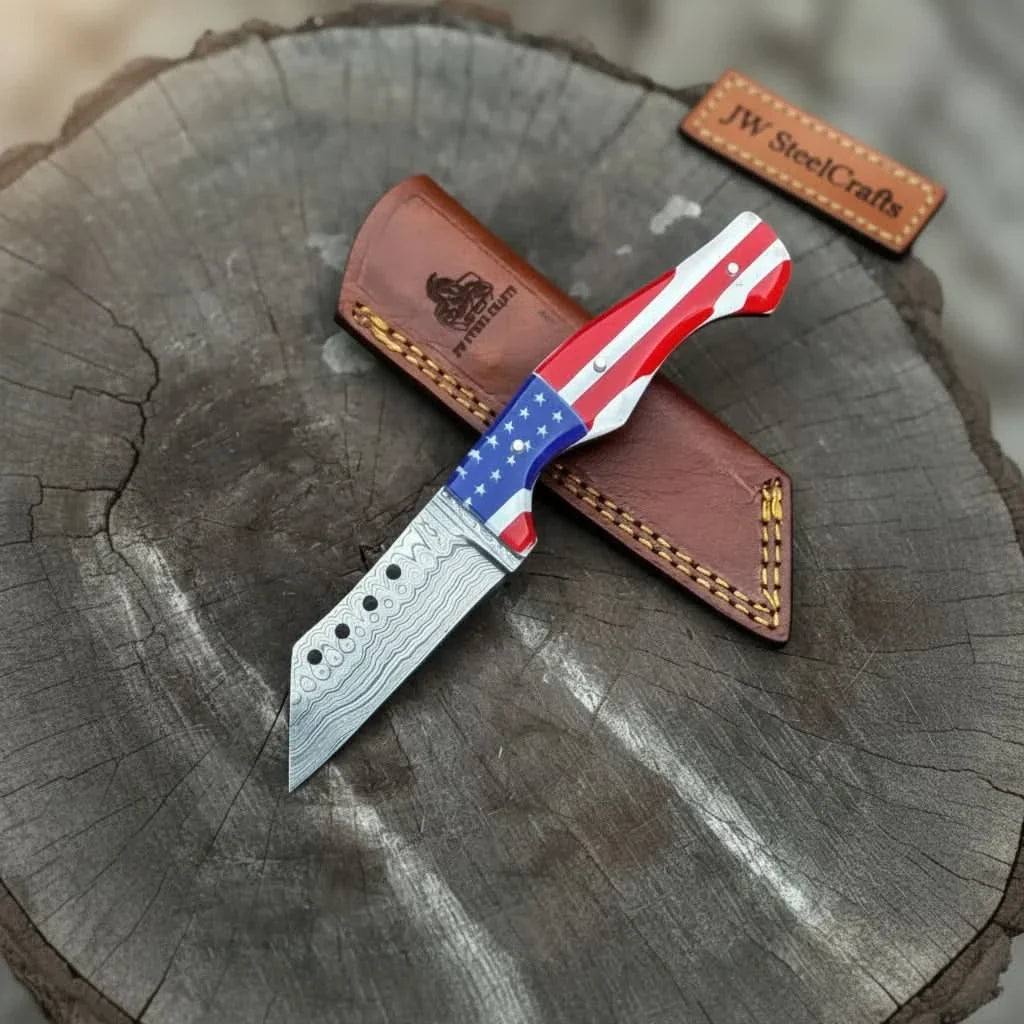 USA Patriotic fixed blade knife with Damascus pattern sitting on a leather sheath on a tree stump, branded 'JW SteelCrafts'.
